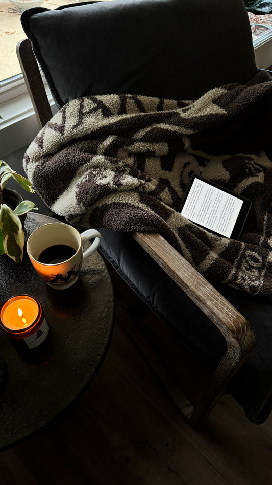 A cozy reading chair with a soft Hogwarts blanket, coffee, and a candle.